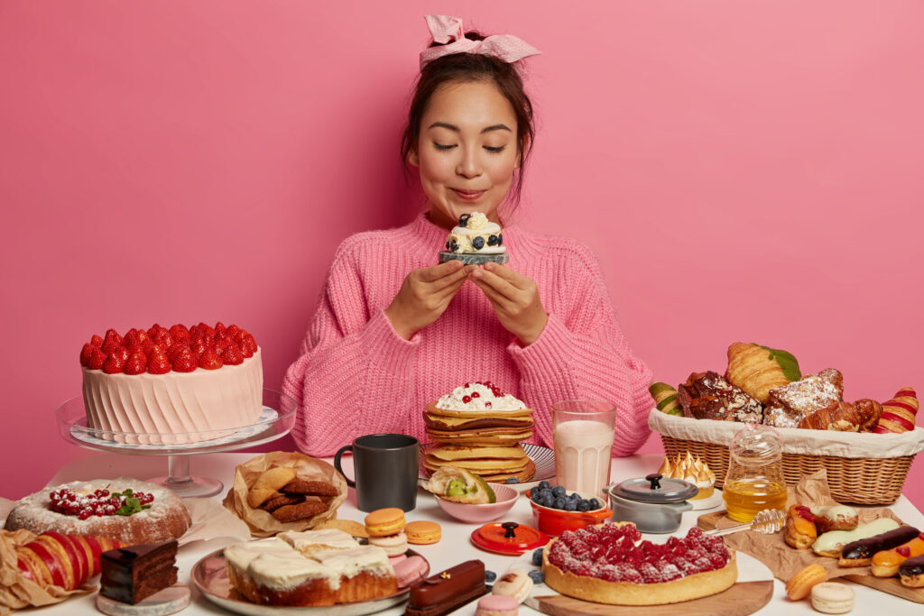 photo of adorable korean woman holds yummy sugary dessert or muffin, isolated over pink background, tastes fresh baked confectionery, cant imagine life without sweet dishes, dressed casually